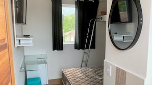 A compact room with a bed, a small desk, a sink, and a TV mounted on the wall. - A5 suites (Ubatuba)