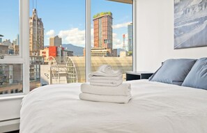 Quarto de hotel com cama, janela com vista para a cidade e um quadro na parede.