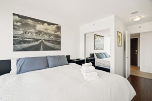 A hotel room with a large bed, a nightstand, a bedside table, a mirror, and a door leading to another room. - Bright 1.5 Bed w/Pool, Parking, HotTub, Sauna, Gym (Vancouver)