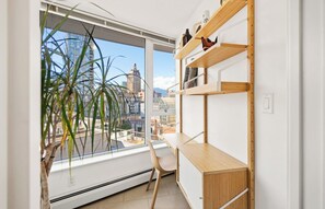 Quarto com uma janela grande, uma escrivaninha, uma cadeira e uma estante de madeira.