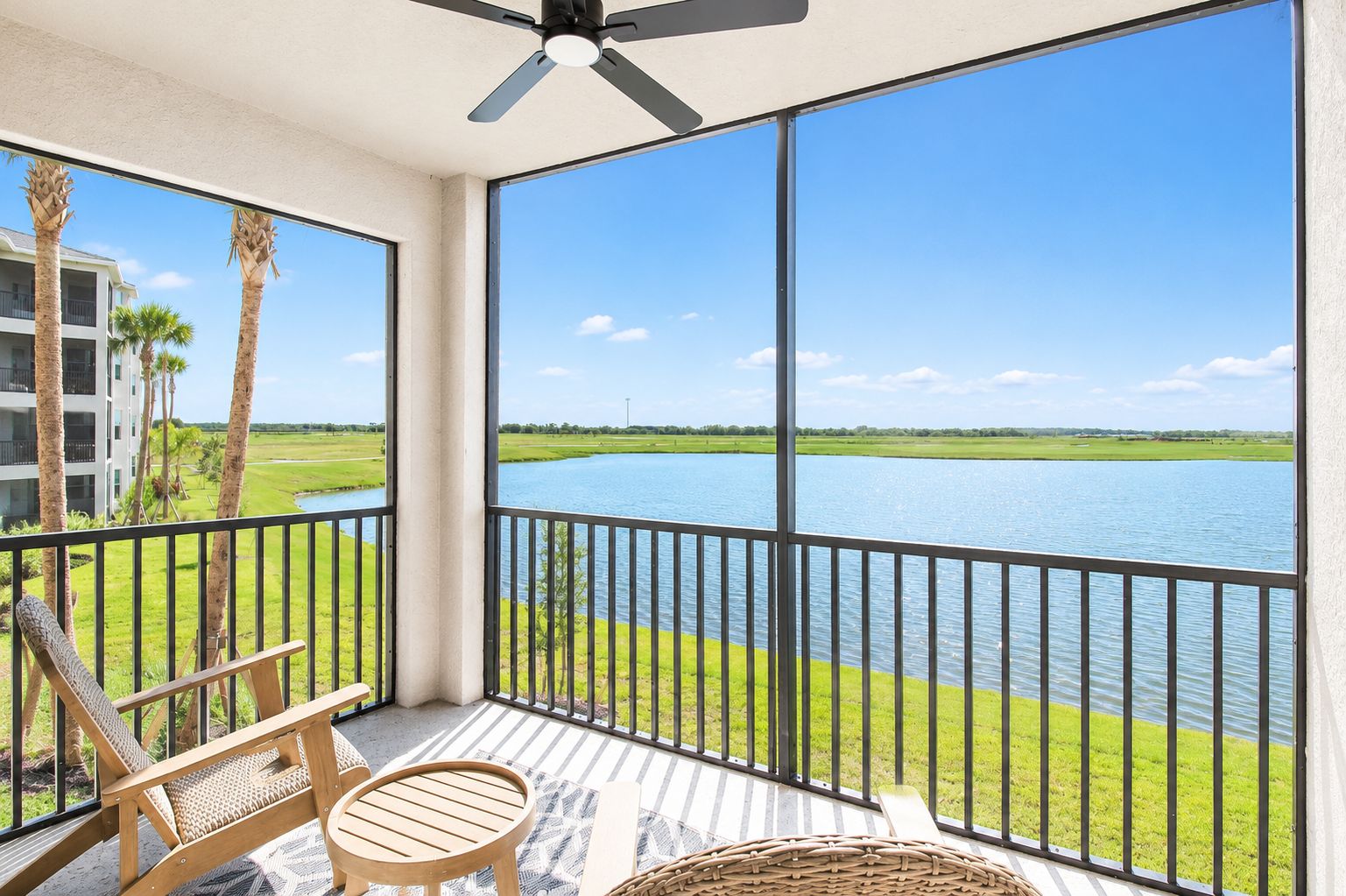 A balcony with a view of a lake, a chair, and a table.