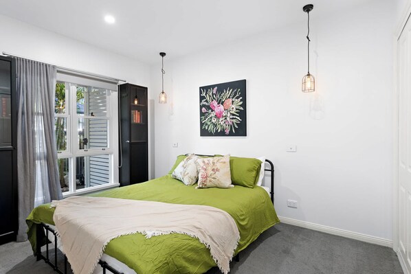 Ein Schlafzimmer mit Bett, einem Fenster mit Vorhängen, einem Wandbild und einer Deckenleuchte.