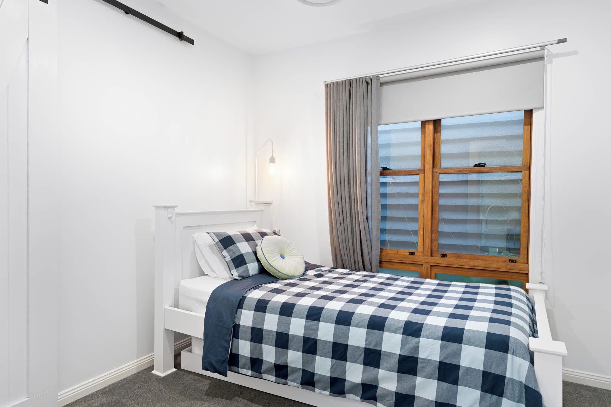A bedroom with a bed, a window with curtains, a bedside table, and a wall-mounted light.