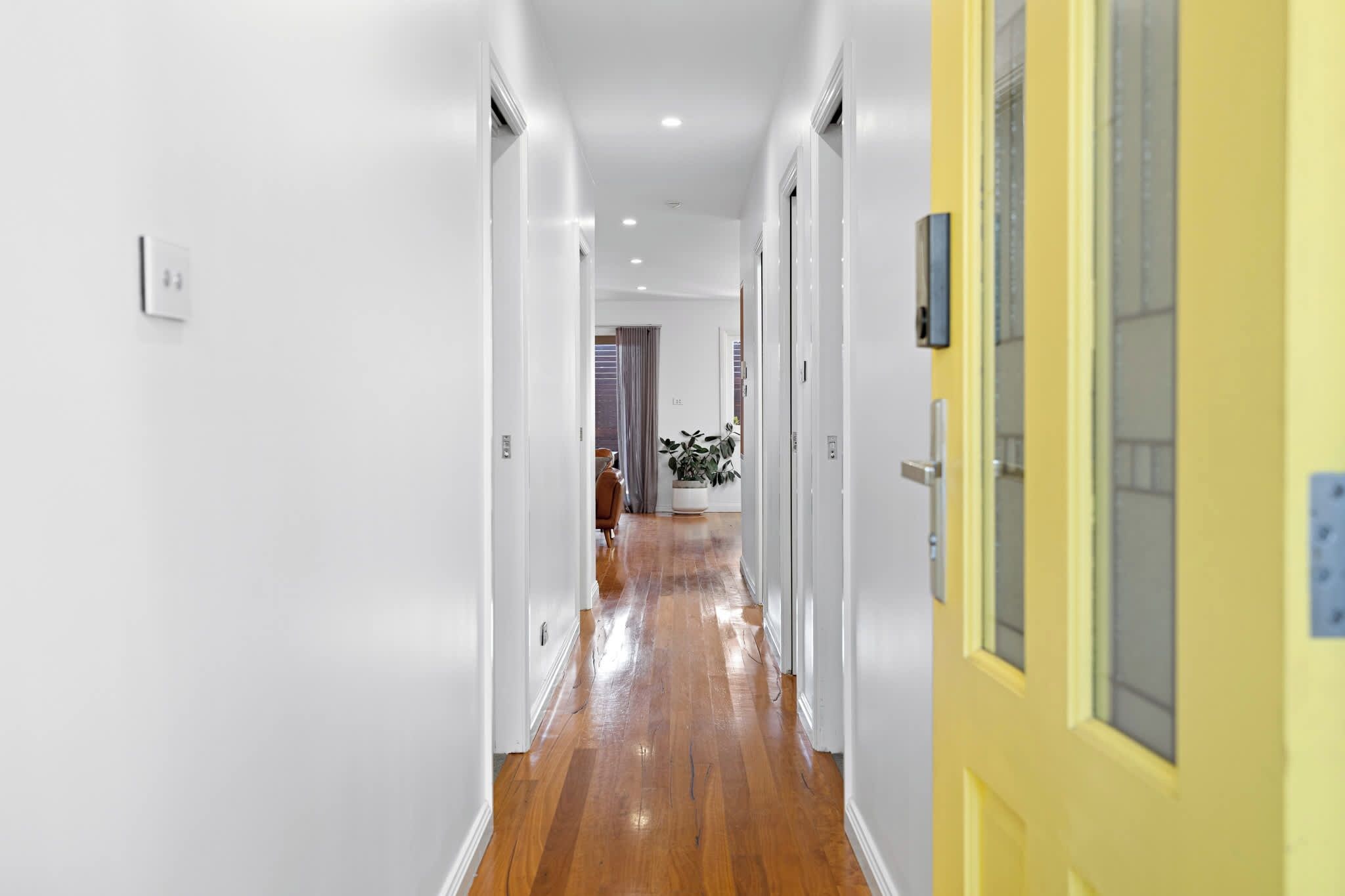 A hallway with white walls, wooden flooring, and a yellow door on the right.