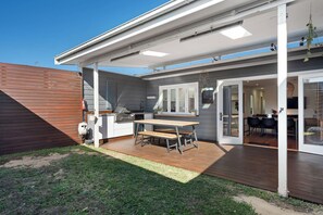 A covered outdoor patio with a wooden table and chairs, a barbecue grill, and a sliding glass door leading to an interior dining area. - Pet-friendly cottage near cafes, pubs and parks (Merewether)