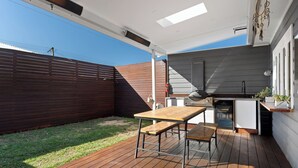 An outdoor patio with a wooden table and chairs, a built-in grill, and a small kitchen area. - Pet-friendly cottage near cafes, pubs and parks (Merewether)