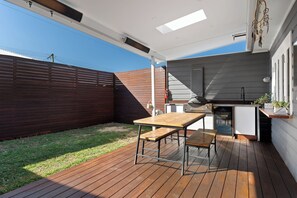 An outdoor patio with a wooden table and chairs, a built-in grill, and a small kitchen area. - Pet-friendly cottage near cafes, pubs and parks (Merewether)