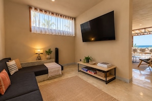 Ein modernes Wohnzimmer mit einer Couch, einem Couchtisch, einem an der Wand montierten Fernseher und einem Fenster mit Vorhängen.