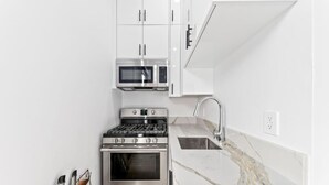 A modern kitchen with white cabinets, a stainless steel stove, a microwave, and a sink with a marble countertop. - Private Guesthouse · Walk to The Grove & LACMA (Los Angeles)