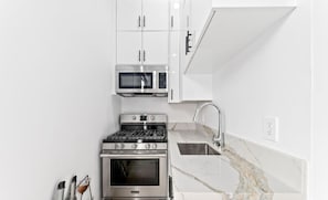 Una cocina moderna con armarios blancos, estufa de acero inoxidable, microondas y un lavamanos con encimera de mármol.