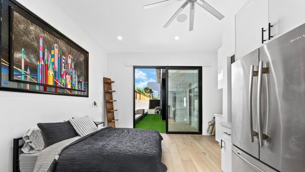 A modern bedroom with a bed, a large painting, a ceiling fan, and a view through a glass door to an outdoor area. - Private Guesthouse · Walk to The Grove & LACMA (Los Angeles)