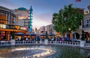 Una plaza pública con una fuente, comercios y una imponente torre del reloj.