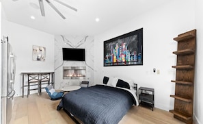 Un dormitorio moderno con cama, chimenea, televisor y estante de madera.
