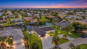 A residential area with houses, a body of water, and a sunset. - Gulf Access Getaway with Heated Pool, Dock, Kayaks and Fun Family Retreat - Salty Serenity - Roelens (Cape Coral)
