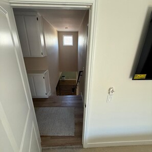 Ein schmaler Flur mit Holzboden, einem kleinen Fenster und einer Tür zu einem Zimmer mit einem Bett.
