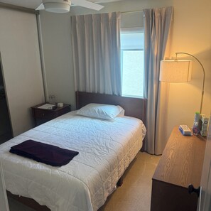 Ein Hotelzimmer mit einem Bett, einem Nachttisch mit Lampe, einem Fenster mit Vorhängen.