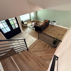 Eine Treppe führt zu einem Wohnbereich mit einer Couch, einem Couchtisch und einem Fenster mit Blick auf Grünflächen.