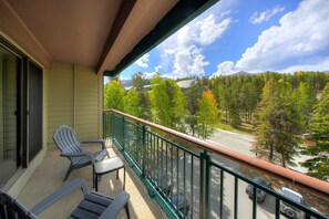 Ein Balkon mit zwei Stühlen, Blick auf eine Straße und ein bewaldetes Gebiet mit einem Berg in der Ferne.