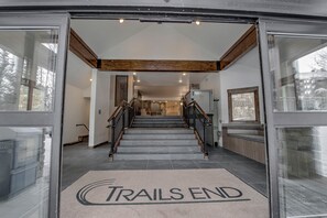 L’entrée d’un hôtel avec un escalier en pierre, des poutres en bois et un paillasson indiquant « FIN DU SENTIER ».