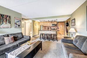 Ein modernes Wohnzimmer mit grauem Sofa, einem Couchtisch und einer Küchenzeile inklusive Mikrowelle und Barhocker.
