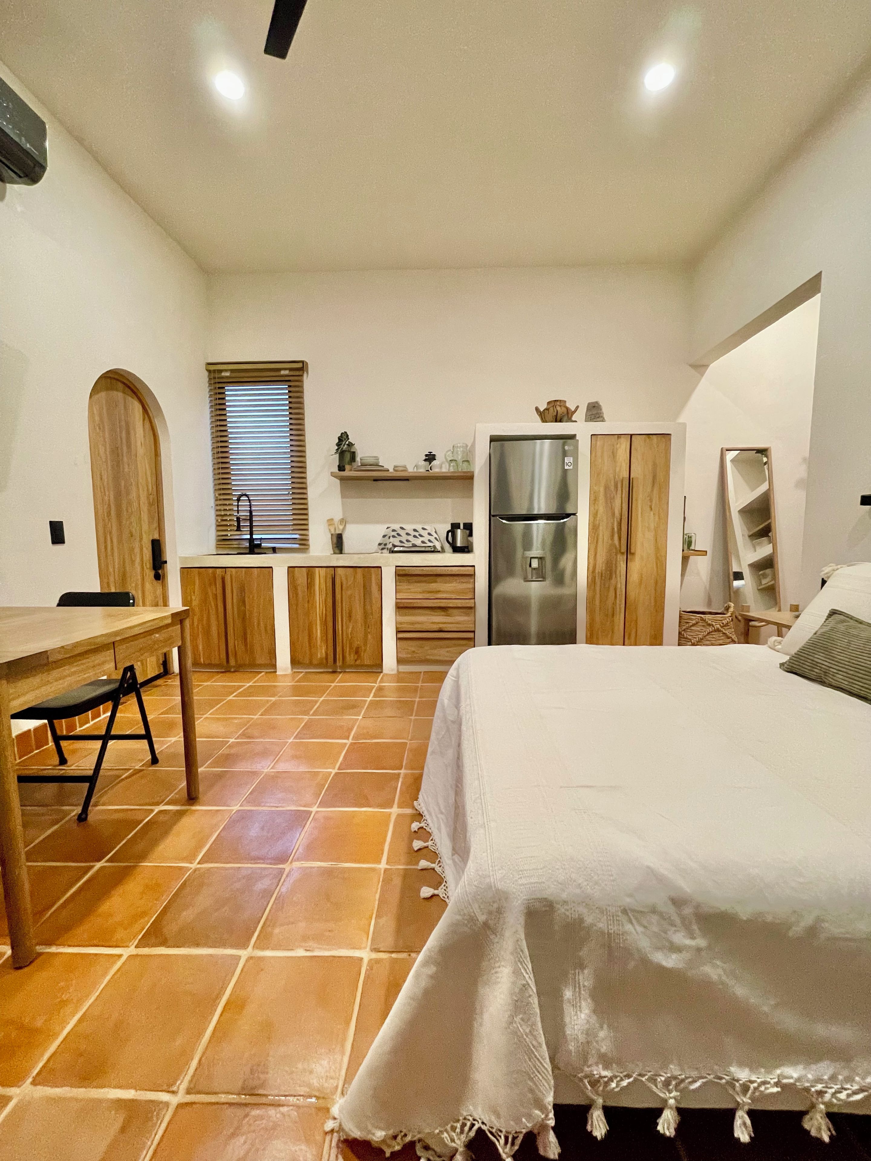 A compact bedroom with a bed, a small table, and a kitchenette area.
