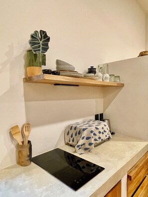 A kitchen with a wooden shelf holding kitchenware, a plant, and a black tablet on the counter.