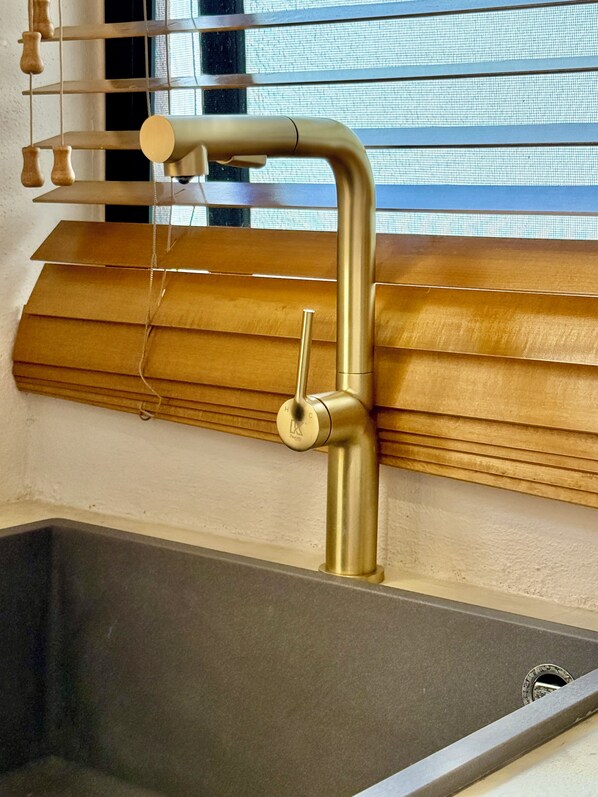 A bathroom with a modern sink, a wooden window blind, and a hanging towel rack.