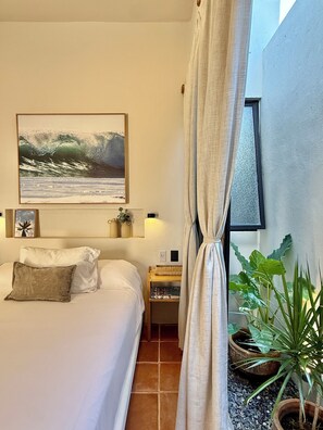 A bedroom with a bed, a painting, a nightstand, a window with curtains, and a potted plant.