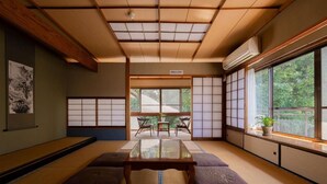Una habitación con tatami, una mesa baja, cojines, puertas correderas shoji y vistas al exterior.