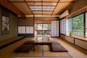 A tatami mat room with a low table, cushions, sliding shoji doors, and a view of greenery outside. - GUESTHOUSE LAPPY (Ureshino)