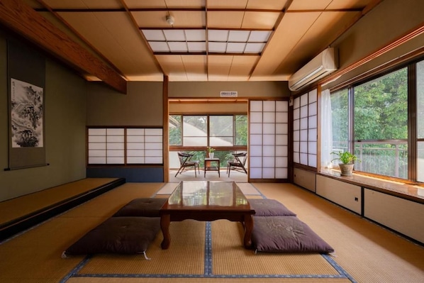 Una habitación con tatami, una mesa baja, cojines, puertas correderas shoji y vistas al exterior.