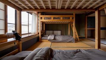 A traditional Japanese-style room with tatami flooring, a futon bed, a wooden bunk bed, and a sliding door.