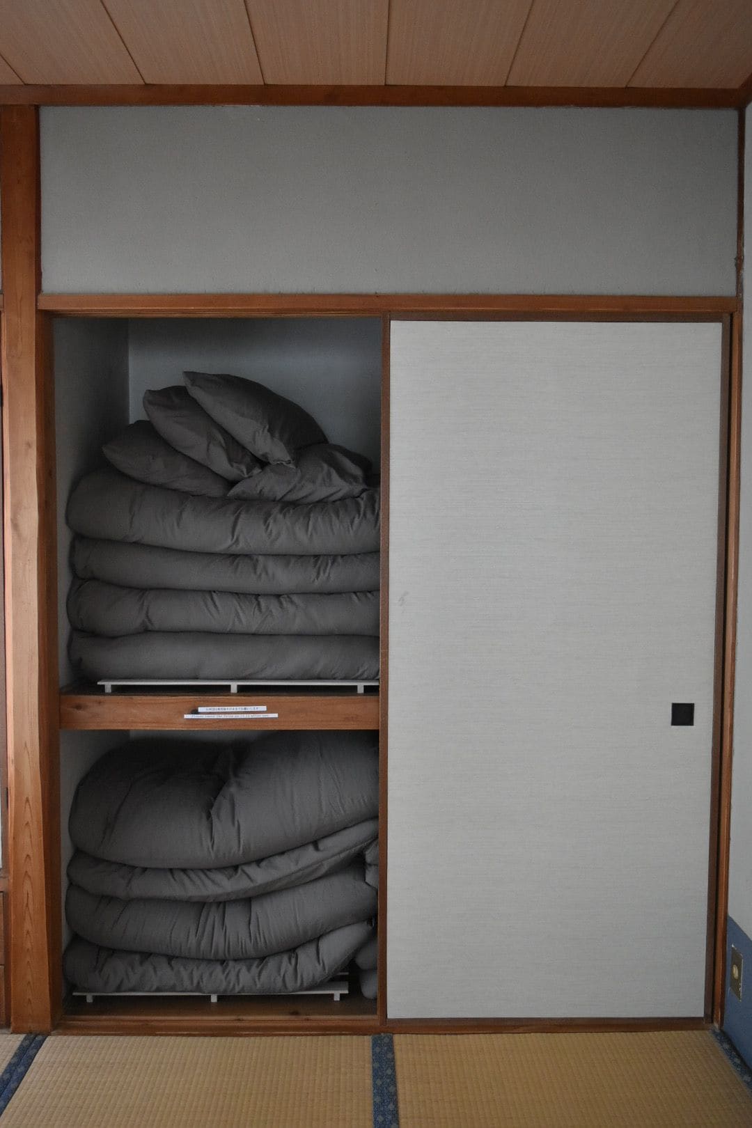 Ein Zimmer mit einem Kleiderschrank, zwei Regalen mit gefalteter Bettwäsche und einem Boden aus Tatami-Matten.