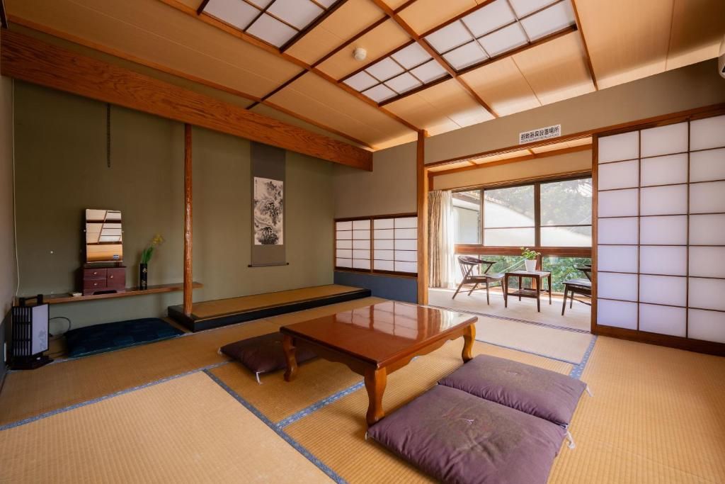 A traditional Japanese room with tatami flooring, a low wooden table, cushions, a sliding door, and a view of the outdoors.