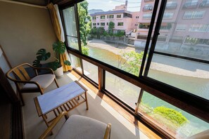 Un balcón con vista a un río, una silla, una mesa y una planta en maceta.