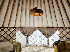 A room with a bed, a sofa, a hanging light fixture, and a window with curtains. - Pohara Coastal View Glamping (Takaka)