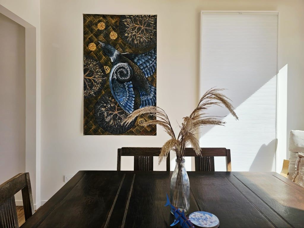 Une table à manger ornée d’un vase contenant des plantes séchées, un tableau accroché au mur et une fenêtre avec des stores.