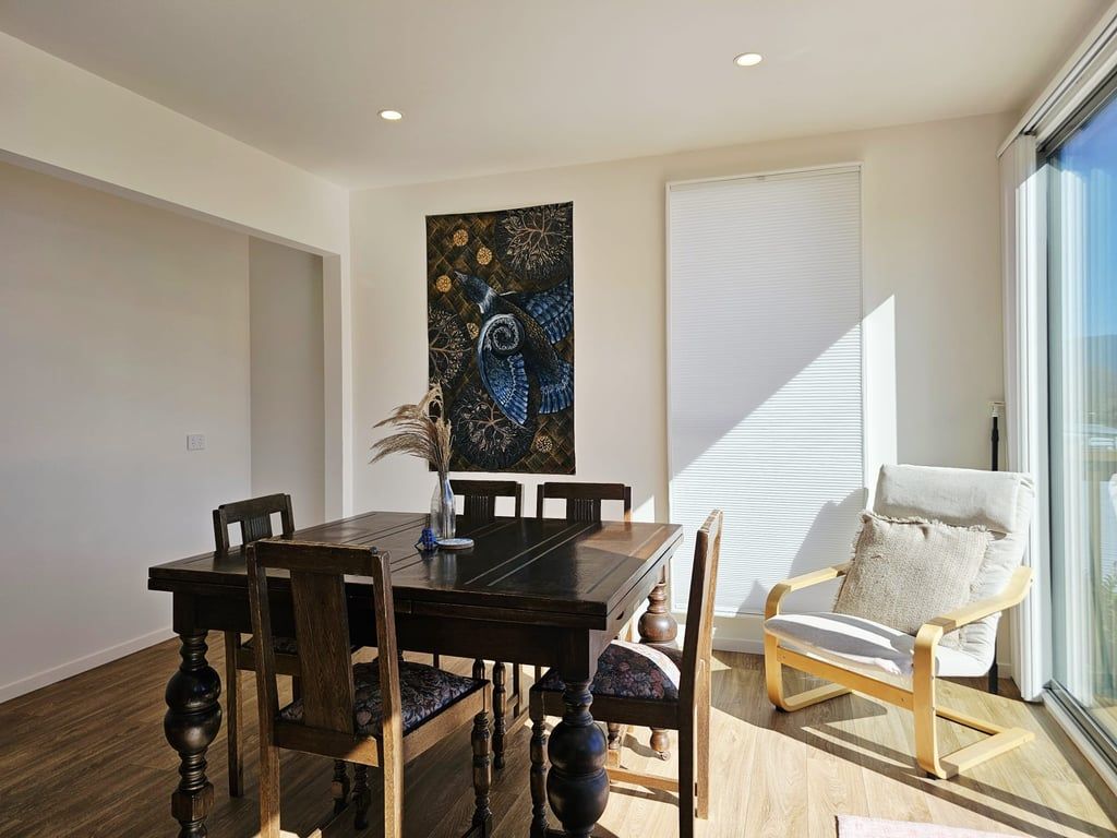 Un coin repas avec une table et des chaises en bois, un élément décoratif mural et une fenêtre avec des stores.