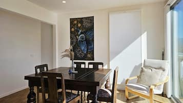Un coin repas avec une table et des chaises en bois, un élément décoratif mural et une fenêtre avec des stores.