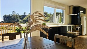 A dining table with a vase of dried plants, a small toy, and a view of a kitchen and outdoor area.