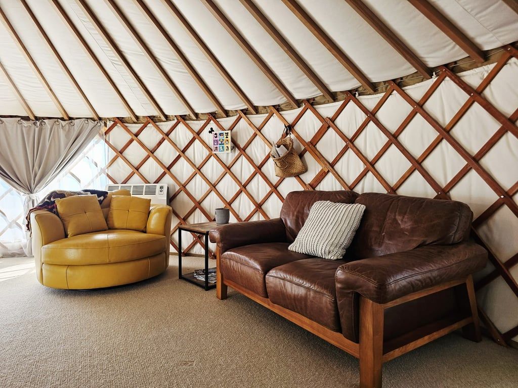 Ein Zeltinnenraum mit einem braunen Ledersofa, einem gelben Sessel und einem kleinen Tisch mit einem Korb.