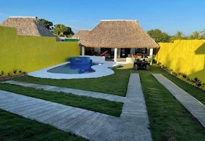 Un área de piscina con un jacuzzi azul, rodeado por una estructura de techo de paja y una pared amarilla.