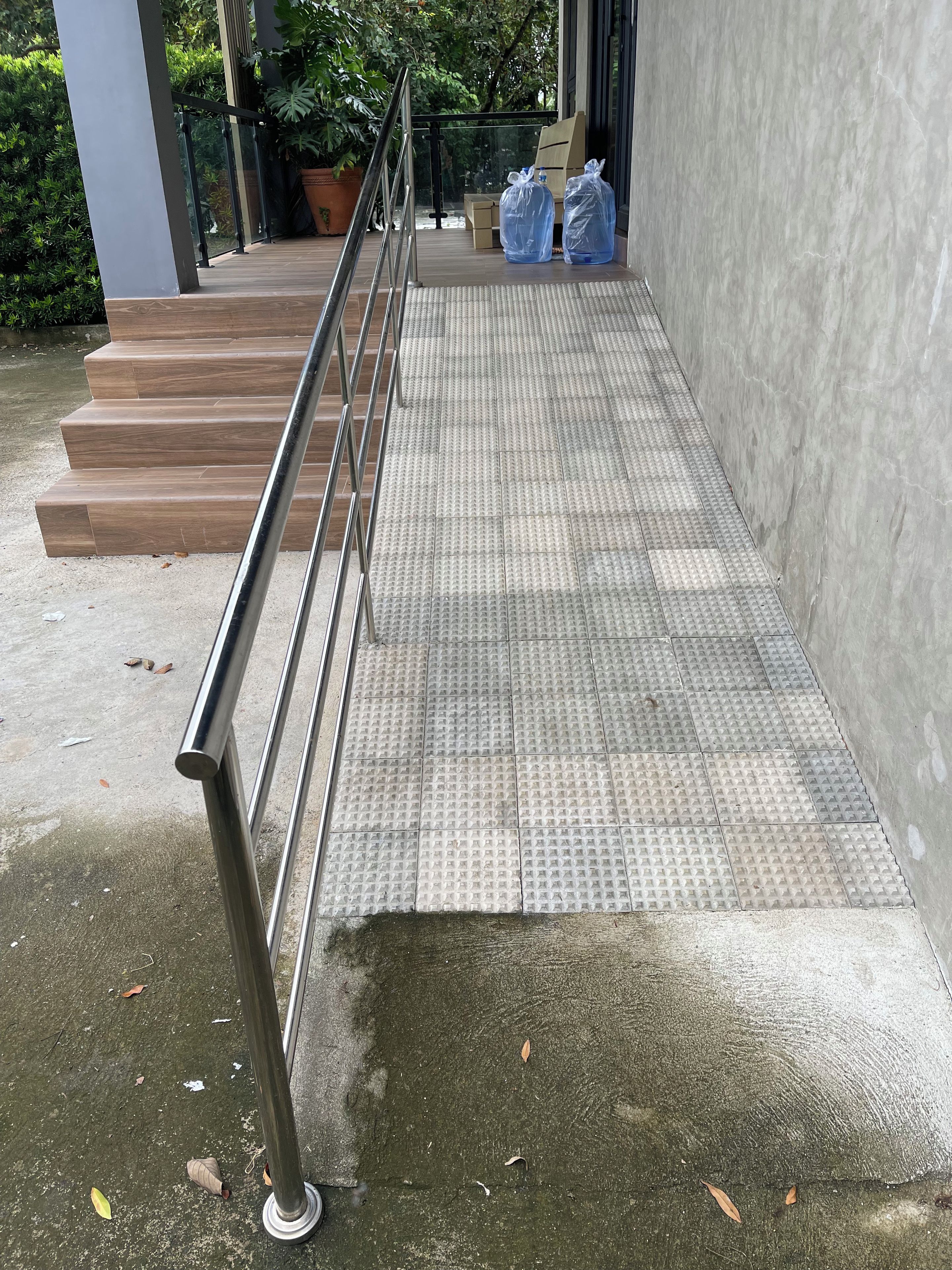 A ramp leading to a building entrance with tactile paving for the visually impaired, a metal handrail, and a concrete floor.
