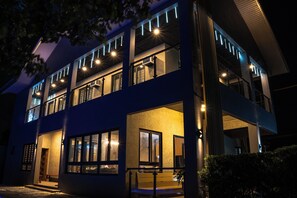A modern two-story building with multiple windows and balconies, featuring a flat roof and a large entrance area.