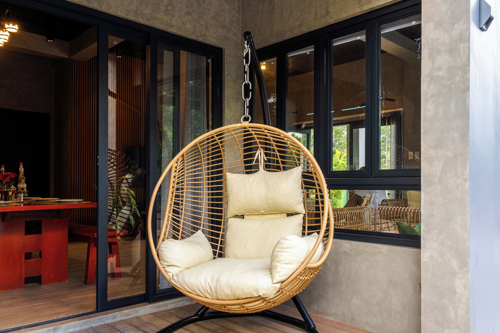 Ein Hängestuhl aus Rattan mit Kissen in einem Zimmer mit großen Fenstern.