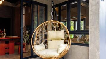 Ein Hängestuhl aus Rattan mit Kissen in einem Zimmer mit großen Fenstern.