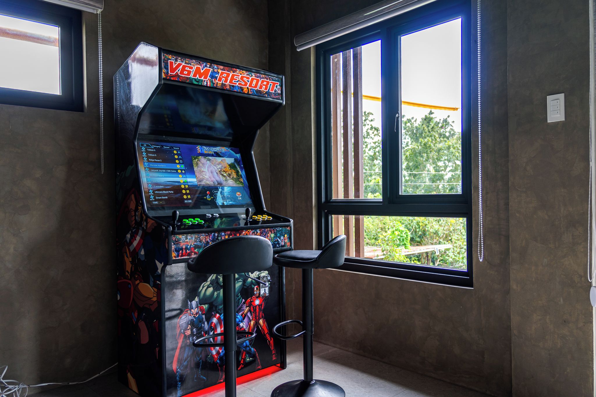 A gaming arcade with a 'VGM RESORT' sign, a bar stool, and a window with a view of greenery.