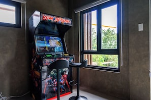 Uma sala de jogos com um letreiro 'VGM RESORT', um banquinho de bar e uma janela com vista para o verde.