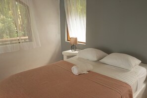 A bedroom with a bed, a bedside table, a lamp, and a window with sheer curtains. - Beachfront Solar Villa - Private Pool - Surf at Your Door - Osa Peninsula (Puntarenas Province)