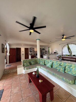 A spacious living area with a large sectional sofa, a wooden coffee table, and two ceiling fans.